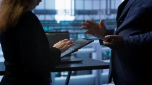 IT security consultants discussing cybersecurity provider options on a tablet in a server room illustrating the questions government contractors should ask before hiring a managed security provider